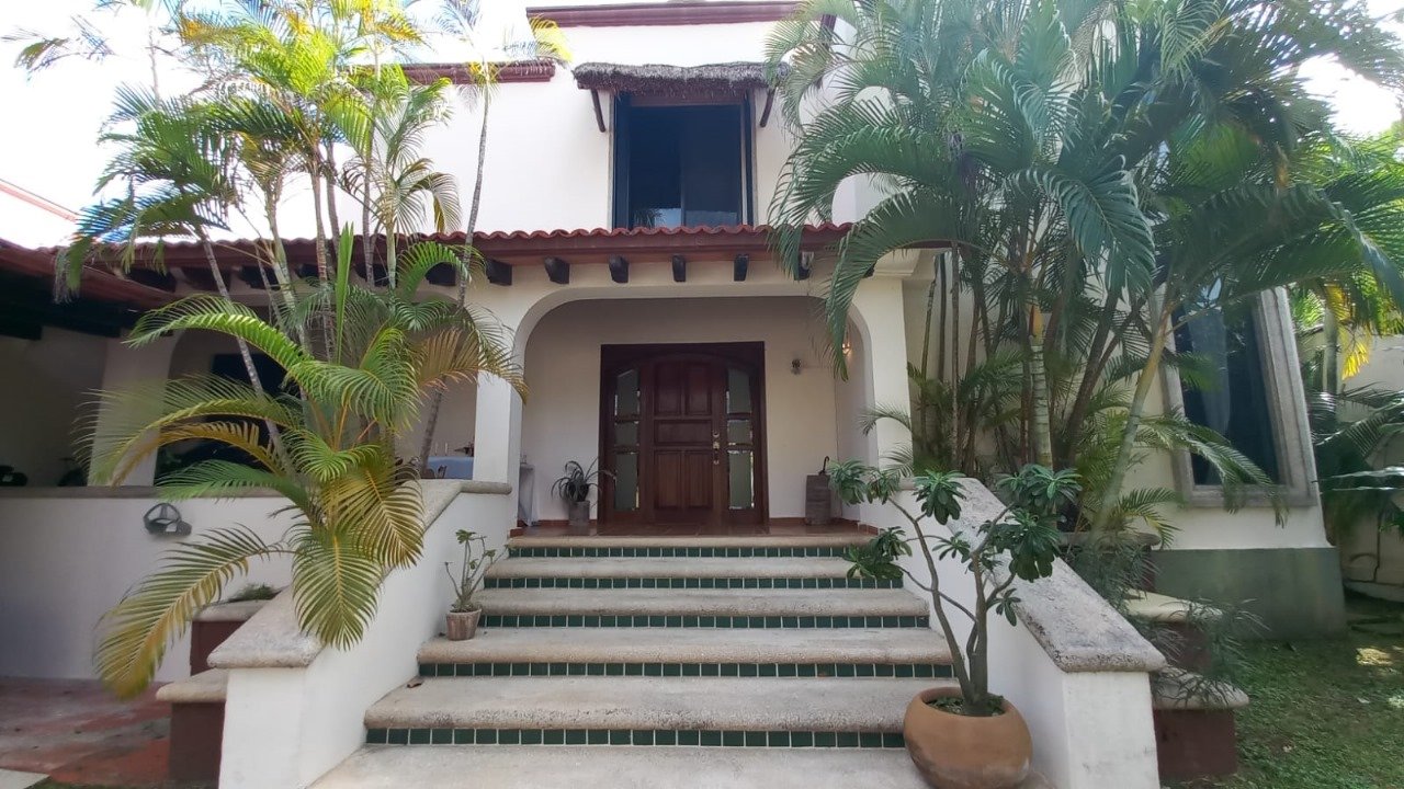 Fachada principal estilo tropical con arcos, techo de teja y palmeras en Residencial Campestre.